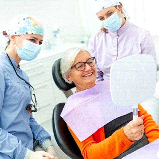 Happy senior dental patient smiling at herself in hand mirror