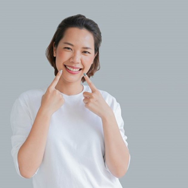 a woman smiling and pointing at her straightened teeth