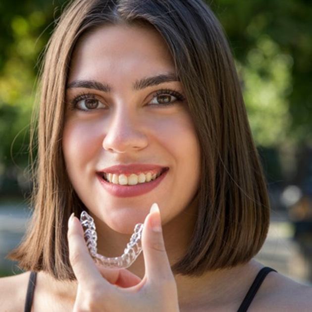 a woman smiling while holding Invisalign aligners