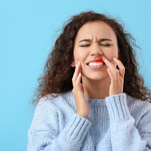 Woman in blue sweater with eyes closed touching inflamed gums in pain