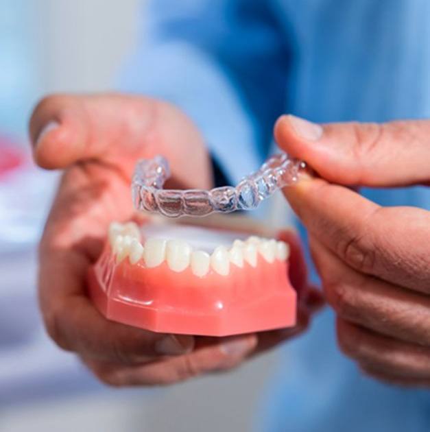 a dentist placing Invisalign aligners on model teeth