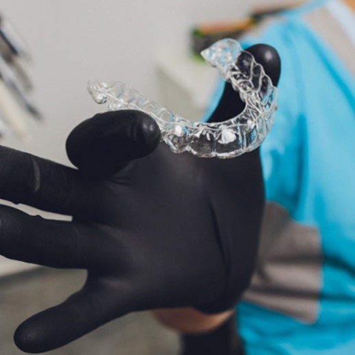 a gloved hand holding Invisalign trays