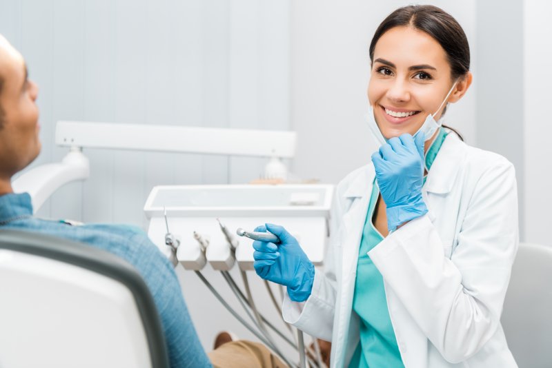 A smiling dentist holding dental tools near her patient