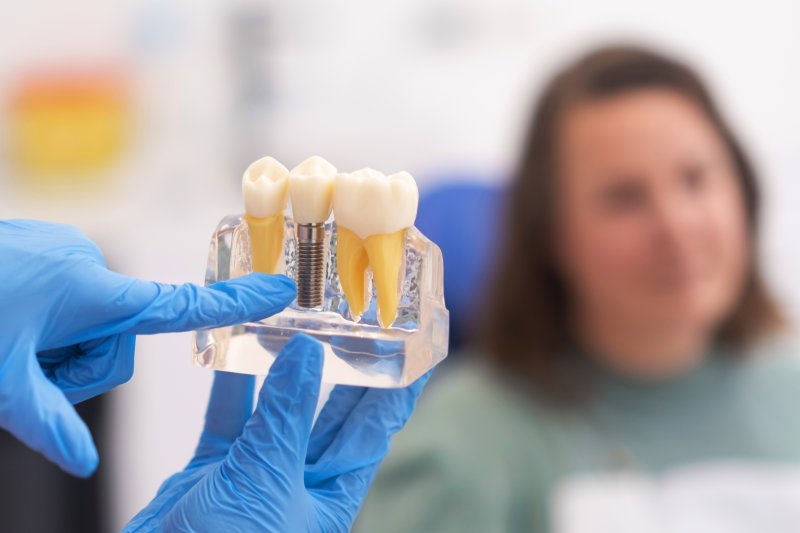 A gloved hand pointing to a dental implant model against a blurred background