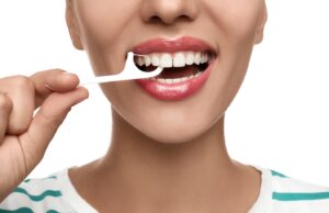 Woman using floss pick to clean her teeth.